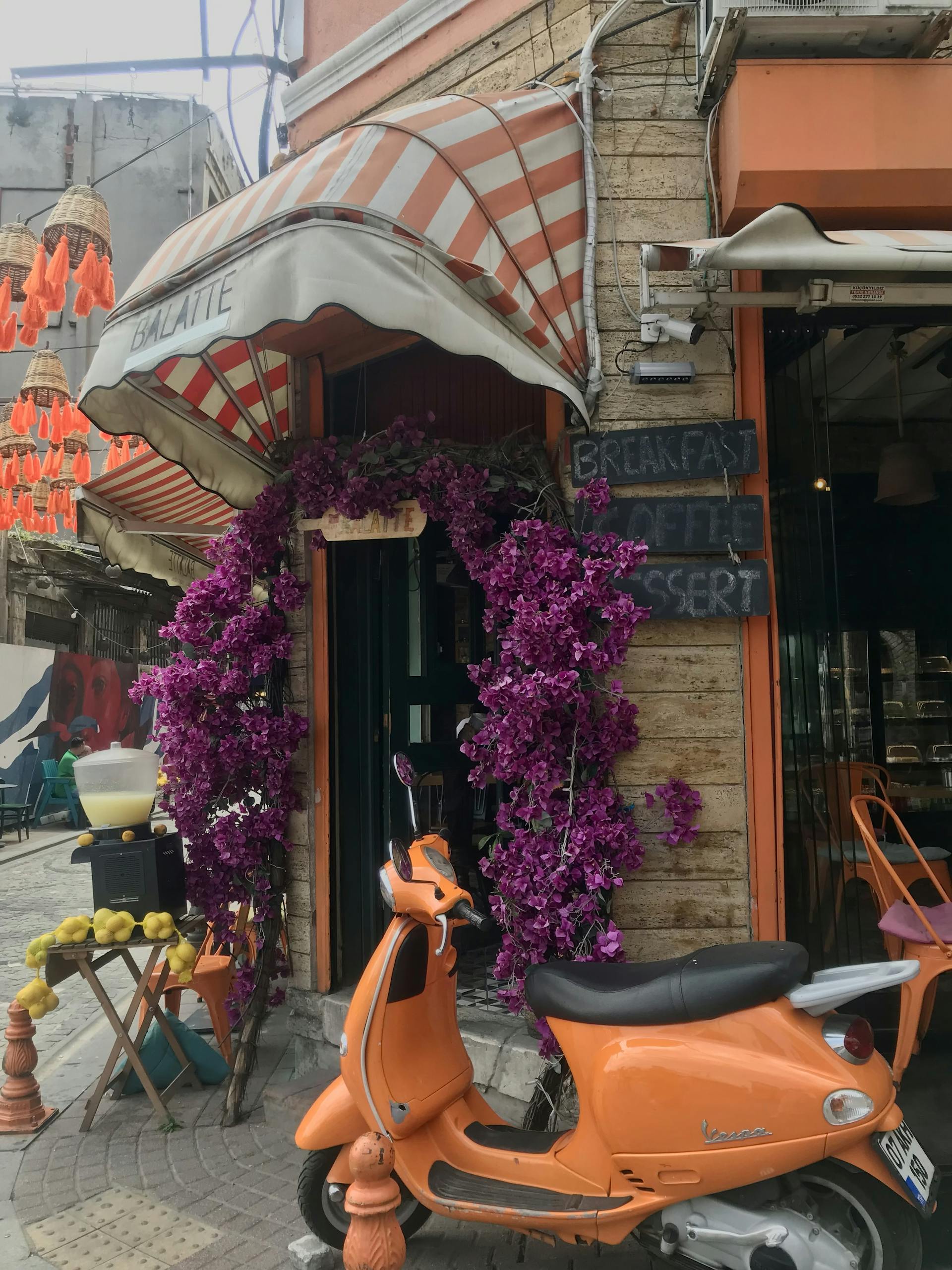 Colorful cafe entrance adorned with flowers and an orange Vespa parked outside.